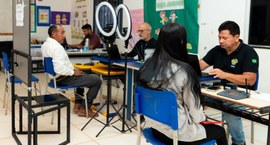 Servidores da Justiça Eleitoral durante atendimento a dois eleitores: uma jovem e um idoso, ambo...