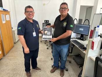 Quatro adultos estão em pé, lado a lado, em um ambiente interno de atendimento público. São dois...