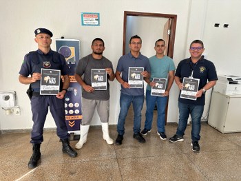 Quatro adultos estão em pé, lado a lado, em um ambiente interno de atendimento público. São dois...