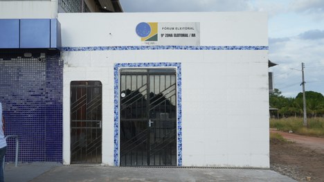 Grupo de cerca de doze adultos posa em pé ao ar livre, em um terreno de terra batida. Eles estão...