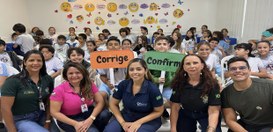 A foto mostra uma sala cheia de estudantes sentados em cadeiras organizadas em filas. Eles veste...