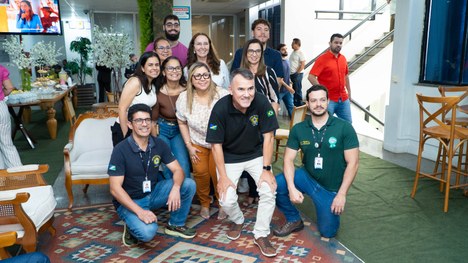 A imagem mostra oito pessoas em pé, alinhadas lado a lado em um ambiente interno que parece ser ...