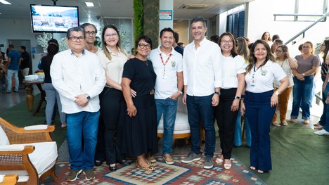 A imagem mostra oito pessoas em pé, alinhadas lado a lado em um ambiente interno que parece ser ...