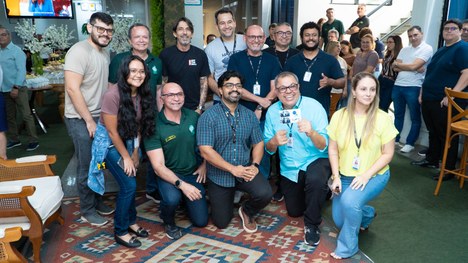 A imagem mostra oito pessoas em pé, alinhadas lado a lado em um ambiente interno que parece ser ...