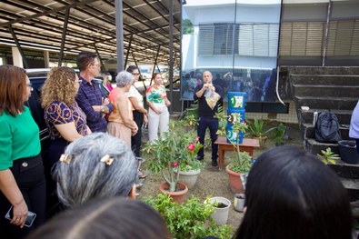 Grupo de pessoas reunido em área externa de um prédio institucional, acompanhando uma demonstraç...