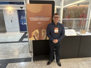 A imagem mostra um auditório cheio, com várias pessoas assistindo a três palestrantes sentados à...