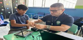 A imagem mostra uma cena em uma sala com carteiras escolares ao fundo. Uma pessoa está sentada à...