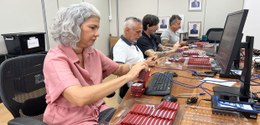 Quatro pessoas sentadas lado a lado em uma sala de trabalho, manuseando e organizando pequenos d...