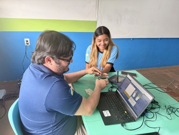 Em uma sala com paredes coloridas em azul, verde e branco, uma pessoa está sentada à mesa operan...
