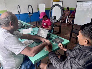 Em uma sala com paredes coloridas em azul, verde e branco, uma pessoa está sentada à mesa operan...