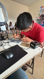 Em uma sala com paredes coloridas em azul, verde e branco, uma pessoa está sentada à mesa operan...