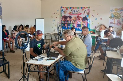 Em uma sala com paredes coloridas em azul, verde e branco, uma pessoa está sentada à mesa operan...
