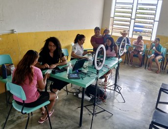 Em uma sala com paredes coloridas em azul, verde e branco, uma pessoa está sentada à mesa operan...