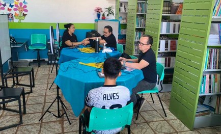 A imagem mostra uma sala organizada como biblioteca, com estantes verdes cheias de livros ao fun...