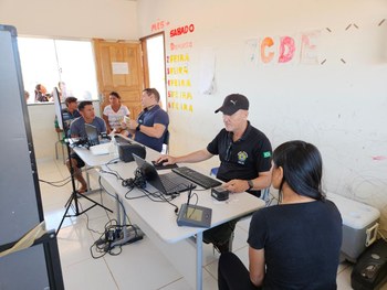 A imagem mostra uma sala organizada como biblioteca, com estantes verdes cheias de livros ao fun...