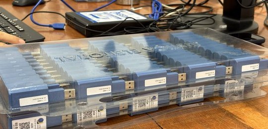 Caixa plástica transparente contendo várias mídias eletrônicas organizadas em fileiras sobre uma...