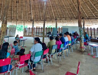 A imagem mostra uma mulher sentada diante de uma câmera com aro de luz, enquanto um servidor ope...