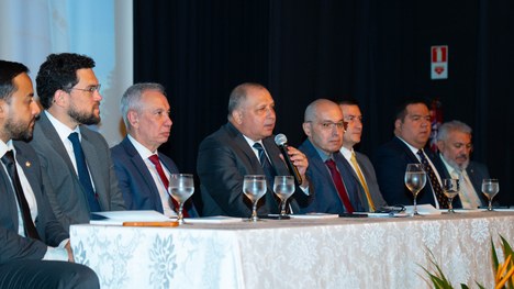 A foto mostra uma mesa comprida, coberta com toalha branca, onde vários homens de terno estão se...