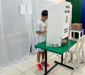 A imagem mostra quatro crianças usando uniformes escolares claros sentadas próximas a uma mesa c...