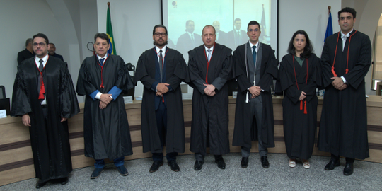 Imagem mostra sete pessoas adultas em pé, lado a lado, usando vestes formais pretas típicas do J...