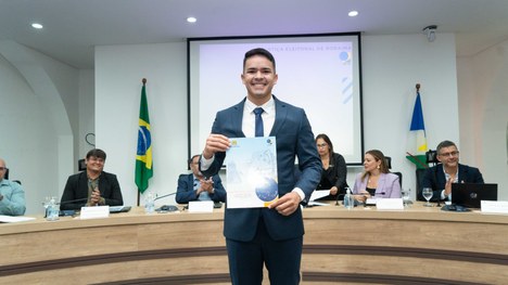A imagem mostra um auditório cheia de pessoas em pé. As cadeiras são vermelhas e estão organizad...
