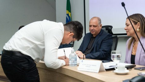 A imagem mostra um auditório cheia de pessoas em pé. As cadeiras são vermelhas e estão organizad...