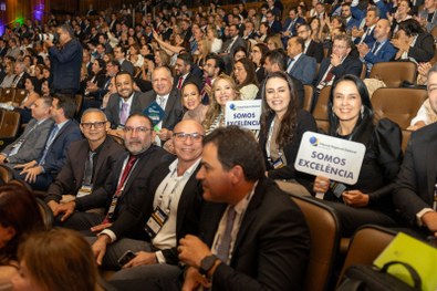 A imagem mostra um homem de terno cinza claro sorrindo e segurando um troféu azul do Prêmio CNJ ...