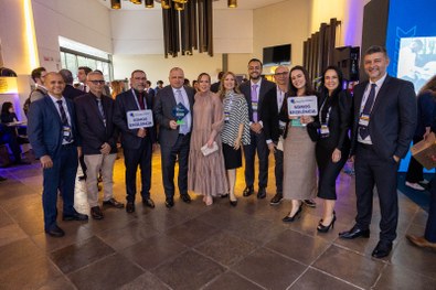 A imagem mostra um homem de terno cinza claro sorrindo e segurando um troféu azul do Prêmio CNJ ...