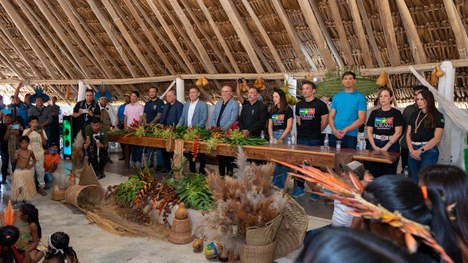 Em uma maloca com cobertura de palha, dezenas de jovens indígenas participam de uma atividade ed...