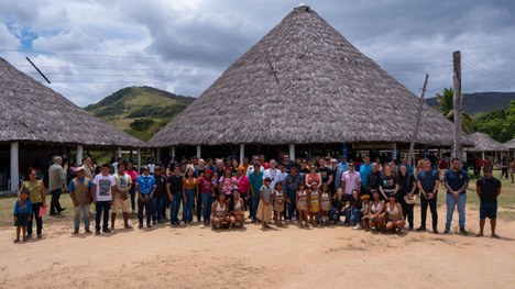 Em uma maloca com cobertura de palha, dezenas de jovens indígenas participam de uma atividade ed...
