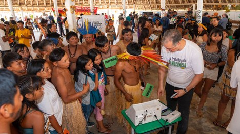 Em uma maloca com cobertura de palha, dezenas de jovens indígenas participam de uma atividade ed...