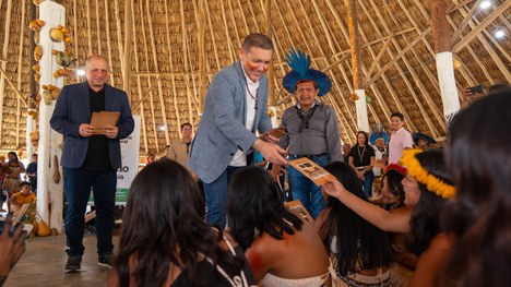 Em uma maloca com cobertura de palha, dezenas de jovens indígenas participam de uma atividade ed...