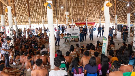 Em uma maloca com cobertura de palha, dezenas de jovens indígenas participam de uma atividade ed...