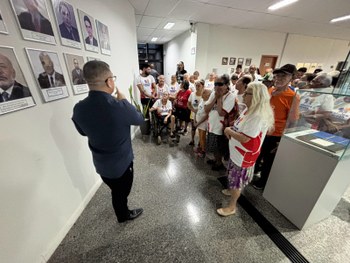 Pessoas visitam o “Espaço Memória TRE-RR”, observando vitrines com documentos e objetos antigos....