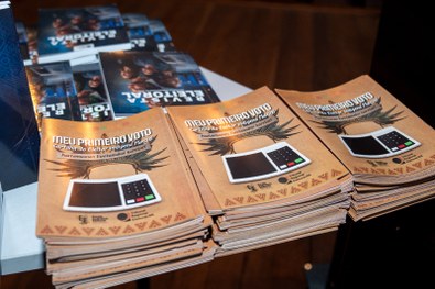 Mesa com várias pilhas de cartilhas organizadas, com capa em tom marrom contendo o texto “Meu Pr...