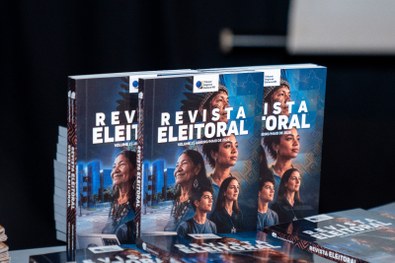Mesa com várias pilhas de cartilhas organizadas, com capa em tom marrom contendo o texto “Meu Pr...