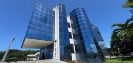 Foto de um prédio moderno do TRE (Tribunal Regional Eleitoral), com fachada de vidro azul espelh...