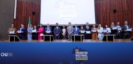 Foto de cerimônia institucional realizada em um auditório. Em um palco, várias pessoas estão ali...