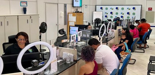 Ambiente interno de atendimento público com vários balcões alinhados. Atrás dos balcões, atenden...