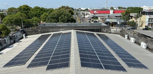 A foto mostra o telhado de um prédio coberto por várias placas solares fotovoltaicas organizadas...