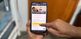 Pessoa segura um celular com uma mão enquanto a outra toca na tela do aparelho. Na tela aparece ...