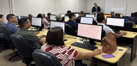 A imagem mostra uma sala de treinamento com várias pessoas sentadas em frente a computadores de ...
