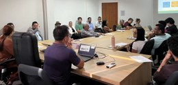 Fotografia de uma reunião realizada em uma sala de conferências moderna e bem iluminada. No cent...
