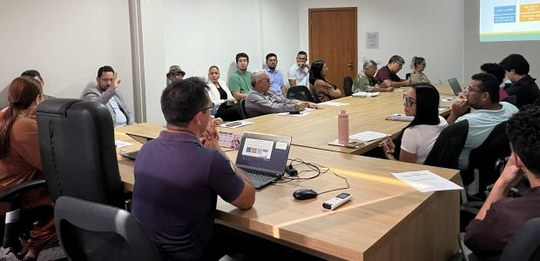 Fotografia de uma reunião realizada em uma sala de conferências moderna e bem iluminada. No cent...