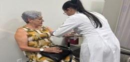 Uma pessoa com cabelo grisalho curto está sentada em uma cadeira, vestindo um vestido sem mangas...