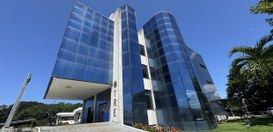 A imagem mostra a fachada de um prédio moderno de três andares, com formato angular e revestido ...