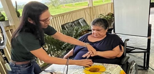 Atendimento domiciliar em área coberta, com uma pessoa sentada em cadeira de rodas enquanto outr...