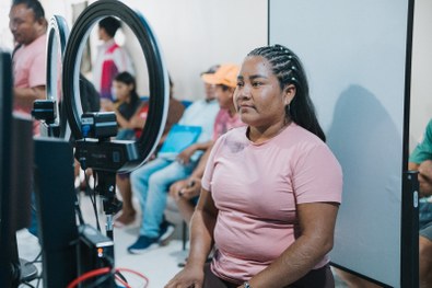 Em um ambiente interno, três pessoas estão posicionadas lado a lado em frente a uma parede clara...