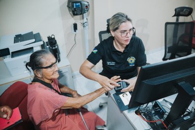 Em um ambiente interno, três pessoas estão posicionadas lado a lado em frente a uma parede clara...