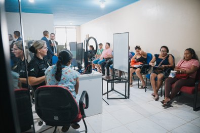 Em um ambiente interno, três pessoas estão posicionadas lado a lado em frente a uma parede clara...